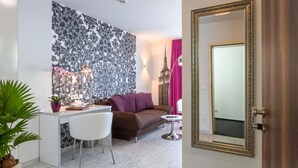 Una sala de estar moderna con un sofá, una mesa de comedor y sillas. Hay un espejo grande en la pared y una planta en maceta en el suelo.