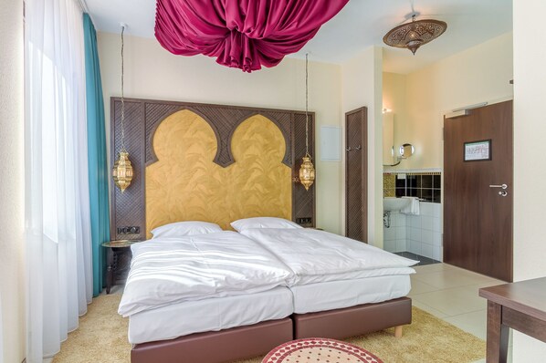 Une chambre d’hôtel avec un grand lit, une tête de lit en bois, deux lampes fixées au mur et une vue sur la salle de bain par une porte ouverte.