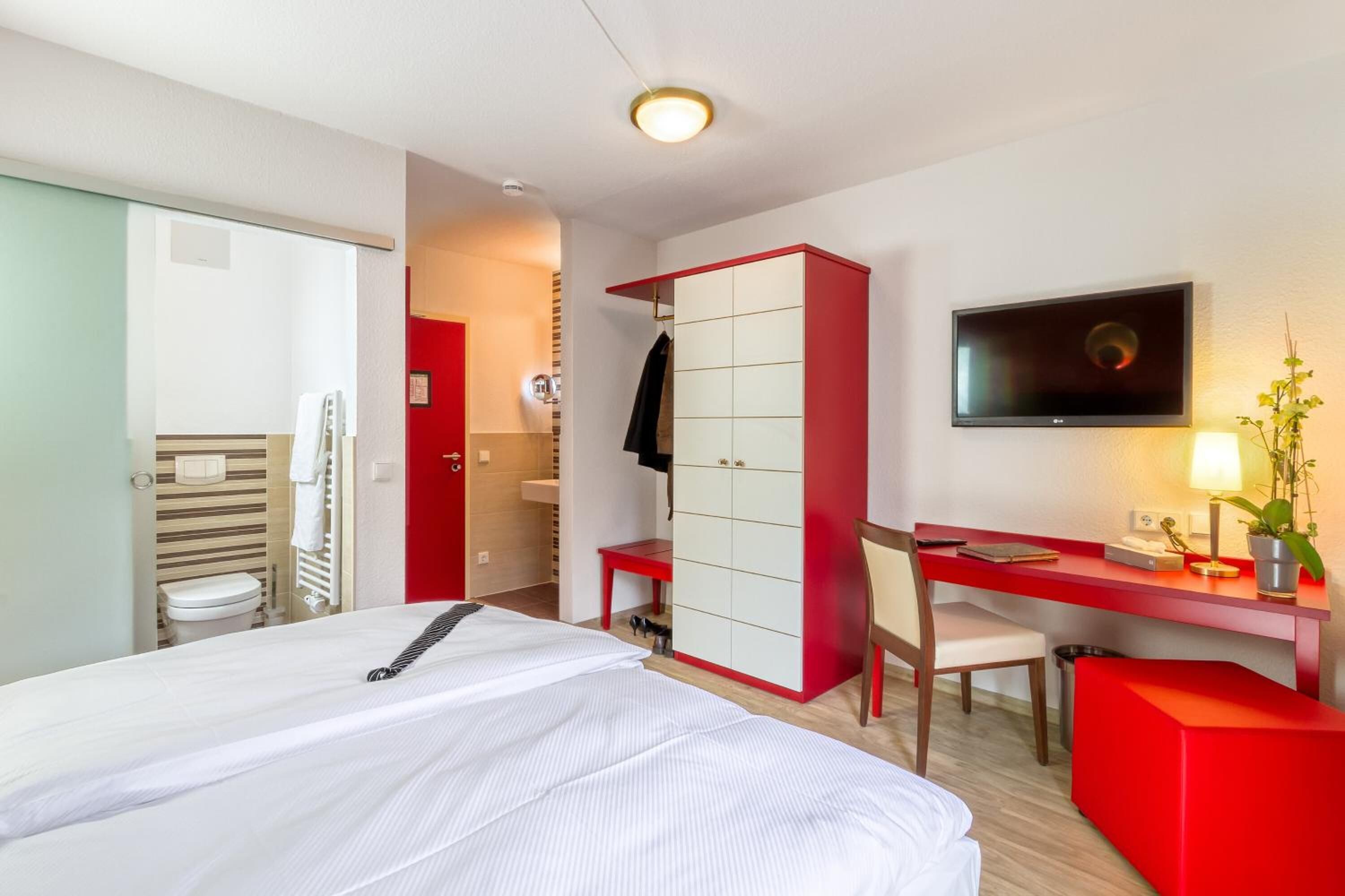 Une chambre d’hôtel avec un lit, un bureau, une télévision et une armoire rouge.
