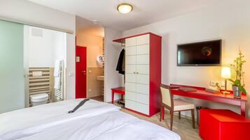 Une chambre d’hôtel avec un lit, un bureau, une télévision et une armoire rouge.
