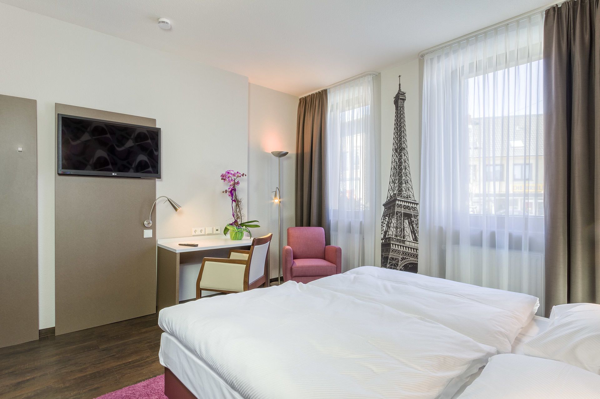 A hotel room with a bed, a desk with a chair, a television, and a decorative Eiffel Tower model.