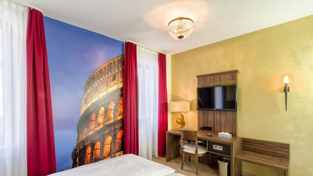 Habitación de hotel con cama, escritorio, silla, televisor y lámpara de pared.