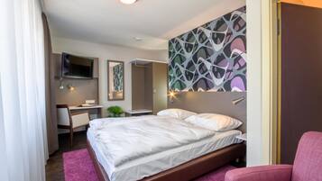 Une chambre d’hôtel moderne, dotée d’un grand lit, d’un bureau, d’une chaise et d’un téléviseur fixé au mur.