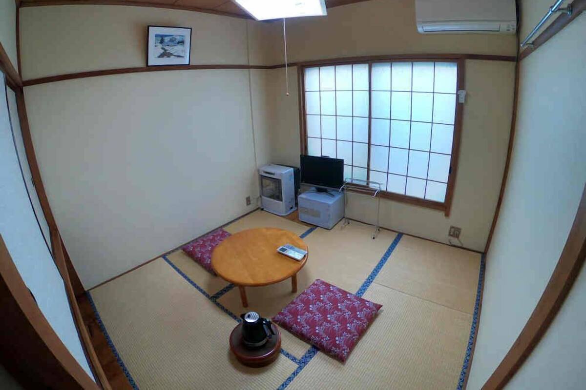 A tatami mat room with a tatami mat table, a television, and a small cabinet.