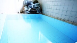 Una bañera con azulejos azules, desagüe, pared de azulejos blancos y una formación rocosa en la esquina.