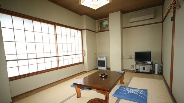 Una habitación tradicional japonesa con suelo de tatami, una mesa de madera baja y un televisor al fondo.