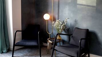 A modern room with two black chairs, a small round table with a vase of flowers, and a tall floor lamp with two spherical lights.