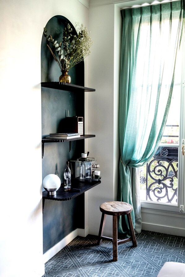 A corner room with a black shelf unit, a small stool, and a window with green curtains. - Grands Boulevards Experimental (Paris)