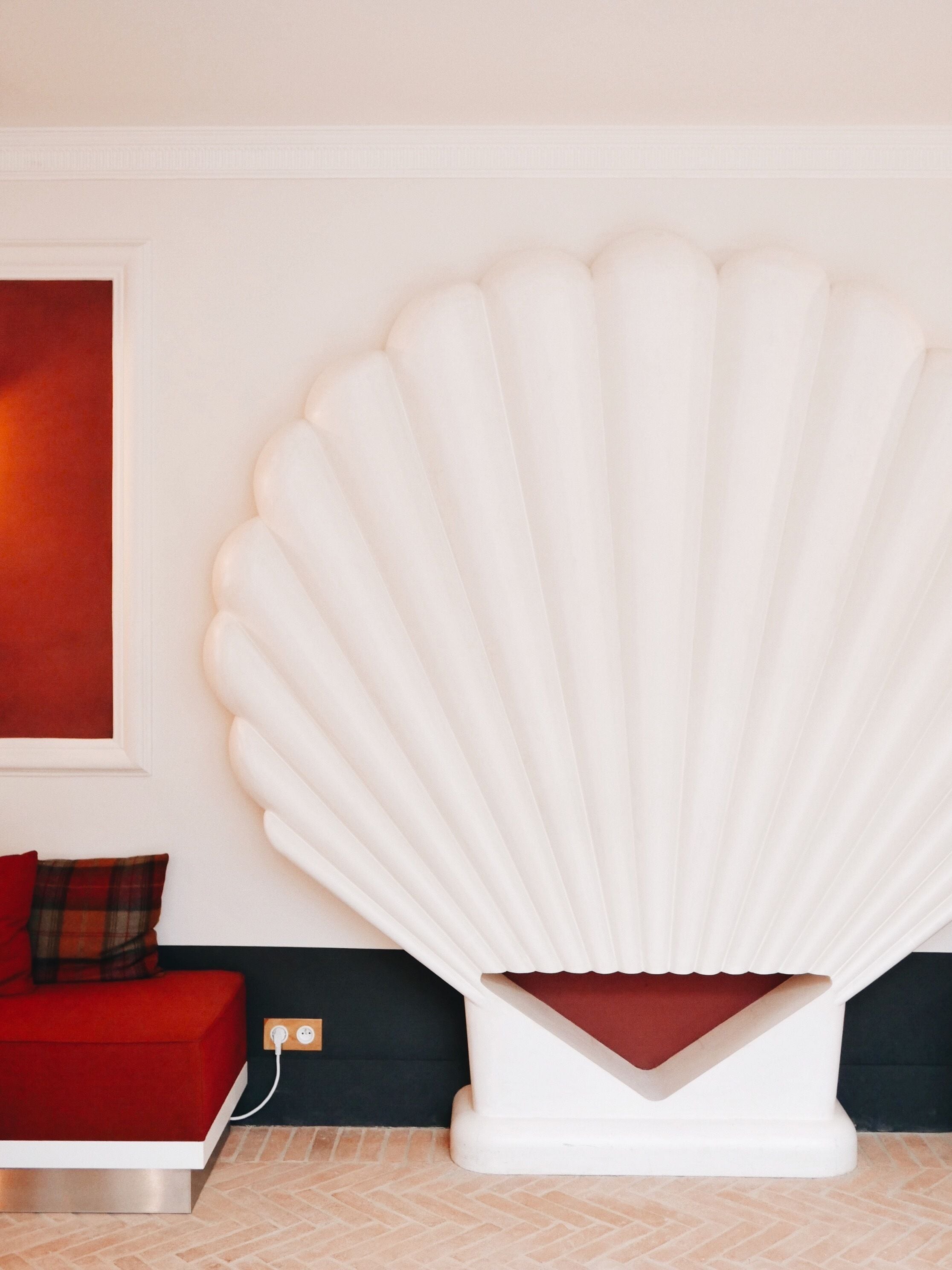 Una habitación moderna con un gran objeto blanco con forma de concha, un sofá rojo y una pared negra.