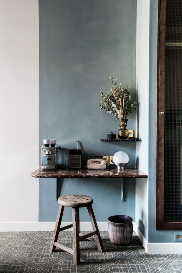 A corner with a dark blue wall, a wooden shelf holding a vintage radio, a vase with dried plants, and a small stool. - Grands Boulevards Experimental (Paris)