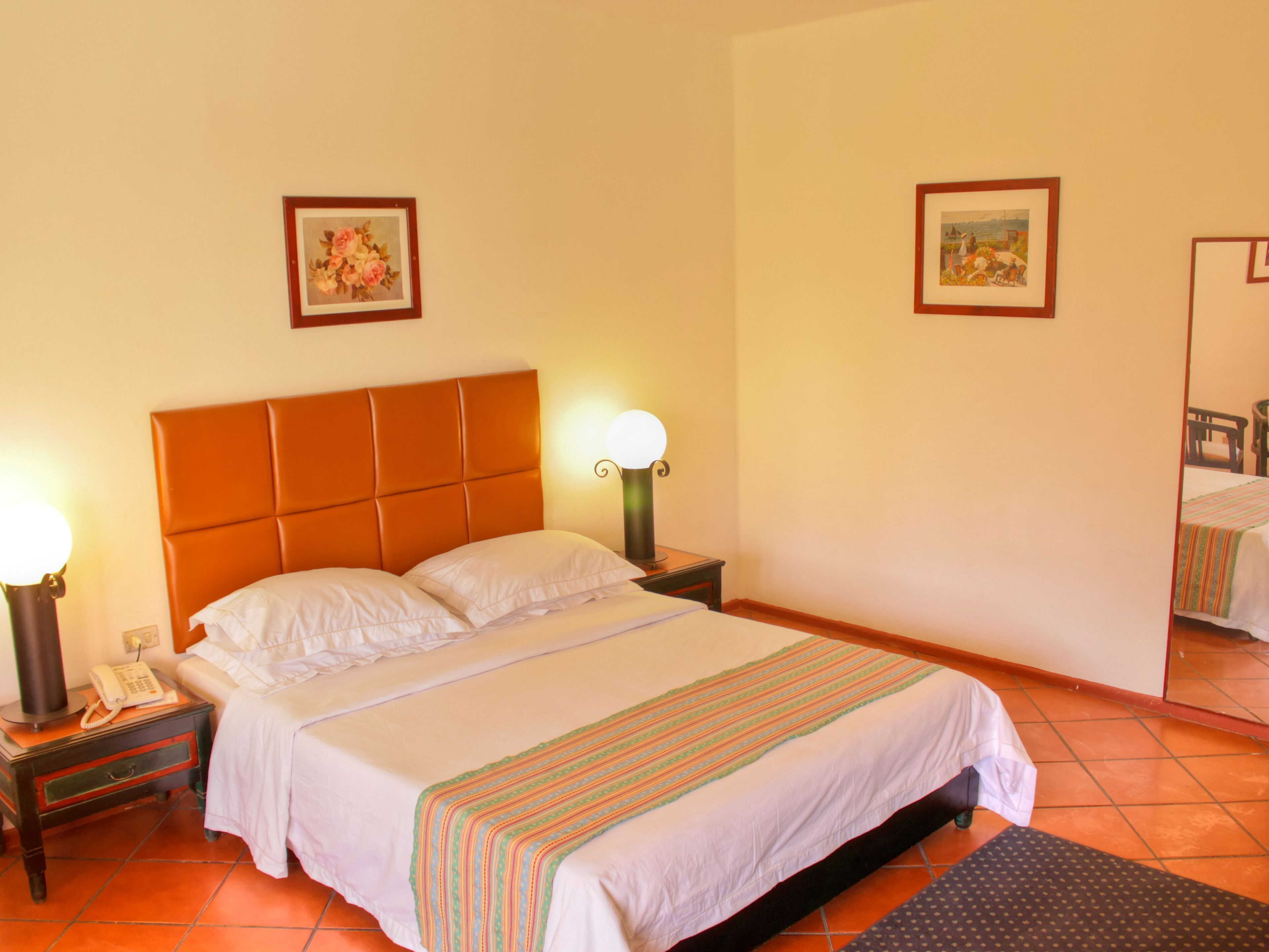Habitació d'hotel amb un llit gran, dues taules de nit, un taulell, un telèfon, dues làmpades penjades a la paret i dos quadres amb marc.