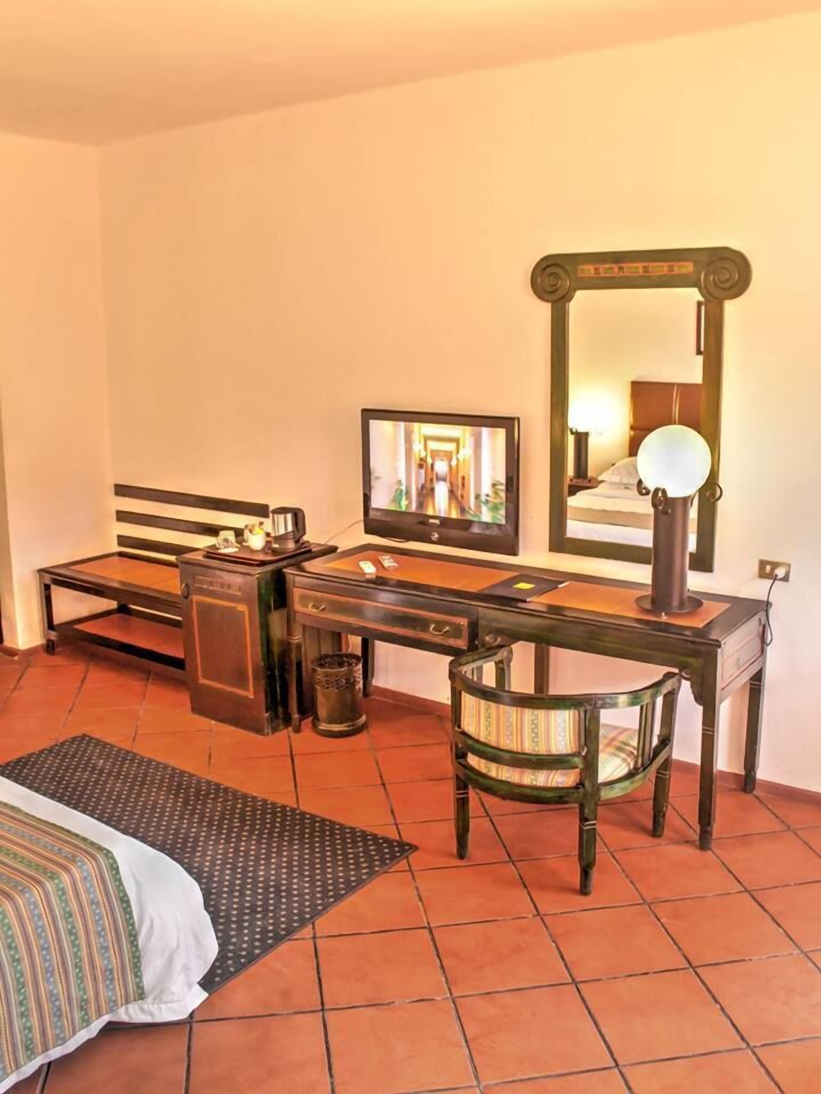 A hotel room with a bed, a desk with a computer, a chair, a mirror, and a television.