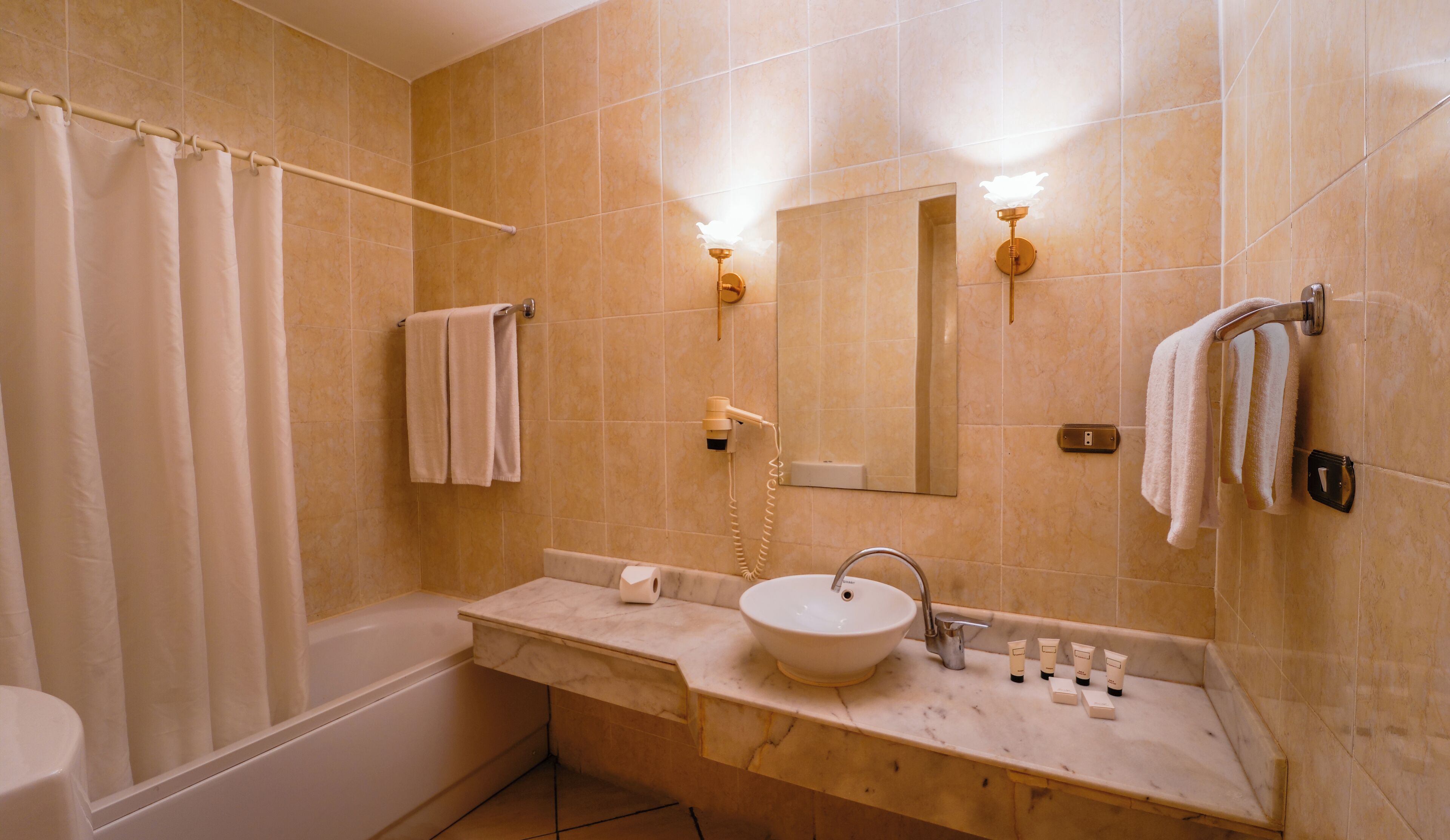 A bathroom with a bathtub, a sink with toiletries, a towel rack, and a mirror.