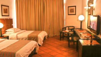A hotel room with two beds, a desk, a chair, a TV, and a large window with curtains.