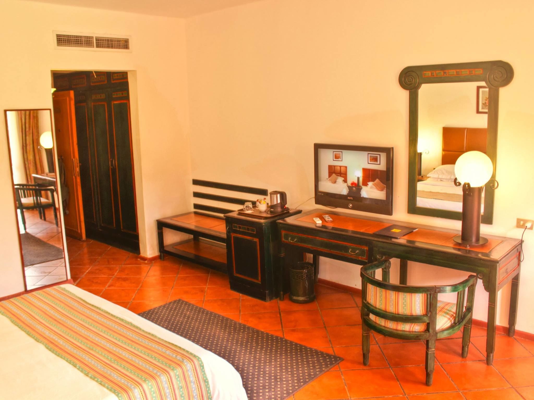 A hotel room with a bed, a desk with a chair, a television, and a mirror.