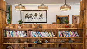 Una estantería de madera llena de libros, un cuadro enmarcado con caligrafía china y una lámpara colgante.