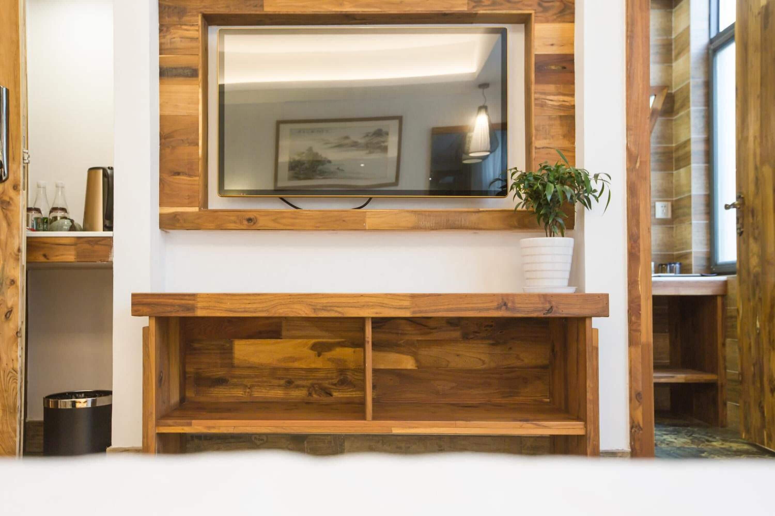 A wooden-framed TV mounted above a fireplace with a potted plant beside it.