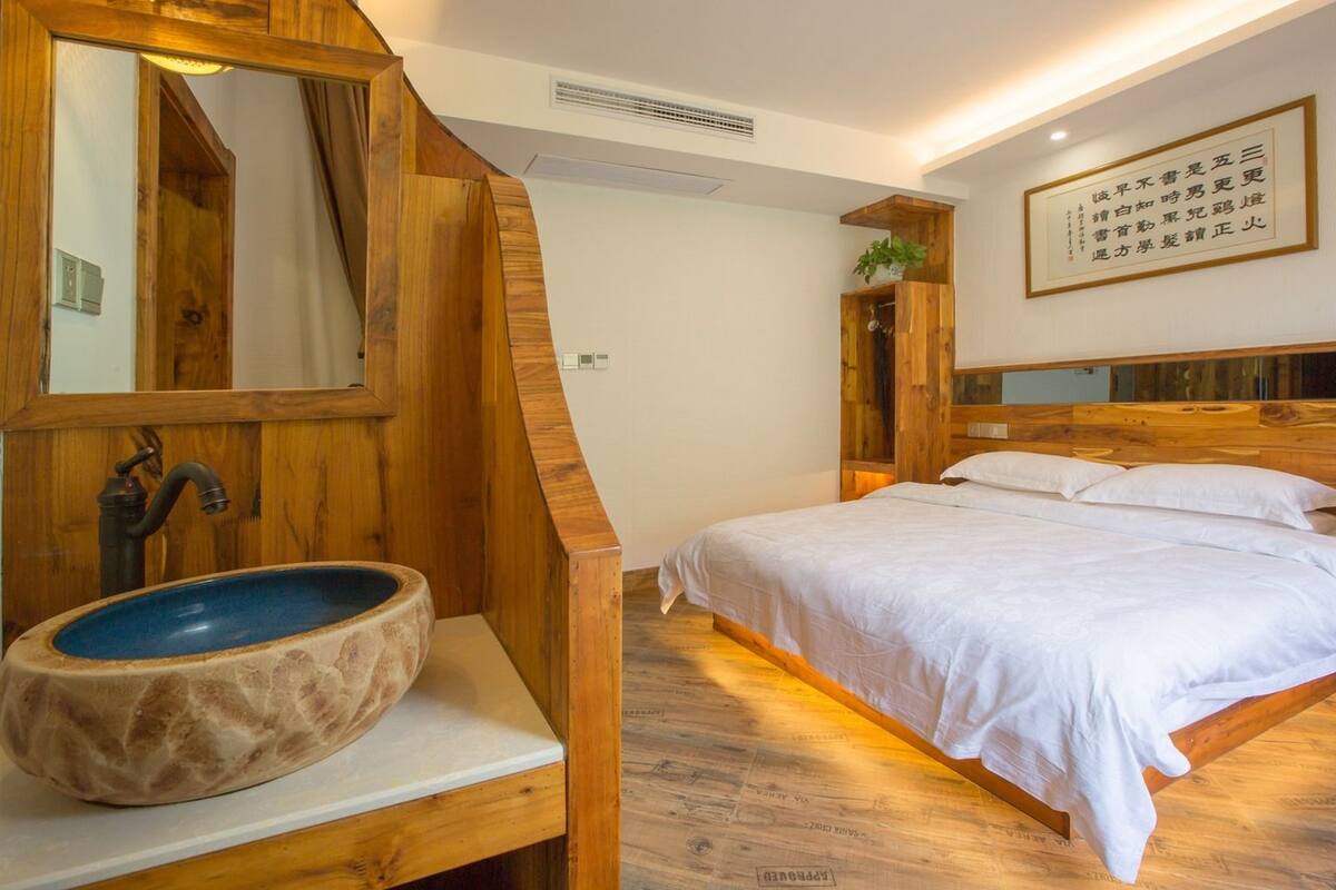 A wooden-framed bedroom with a large bed, a wooden sink, and a mirror.