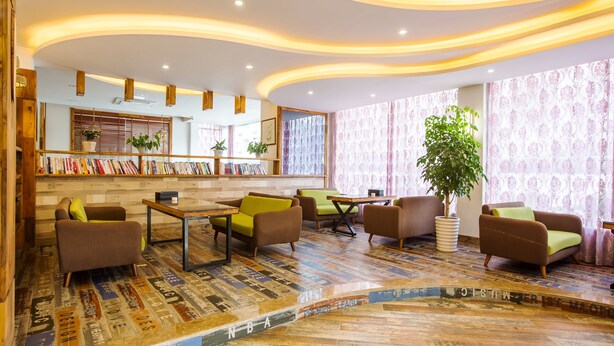 Un área de estar moderna con techo curvo, estanterías de madera, asientos cómodos y suelo estampado.