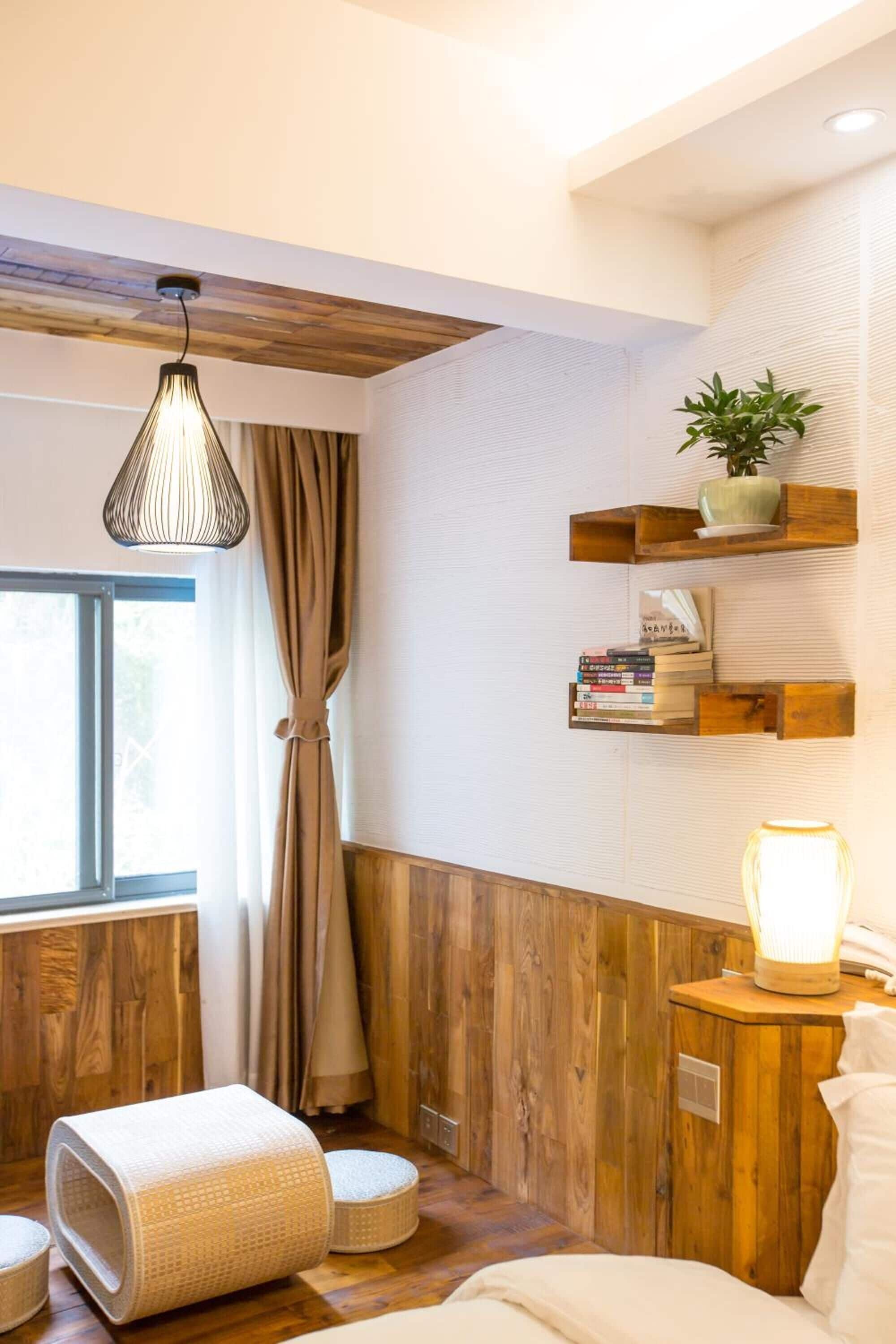 Ein gemütliches Zimmer mit Holzwandverkleidung, einem Bett, einer Leselampe, einem Fenster mit Vorhängen und einem Regal mit Büchern und einer Pflanze.