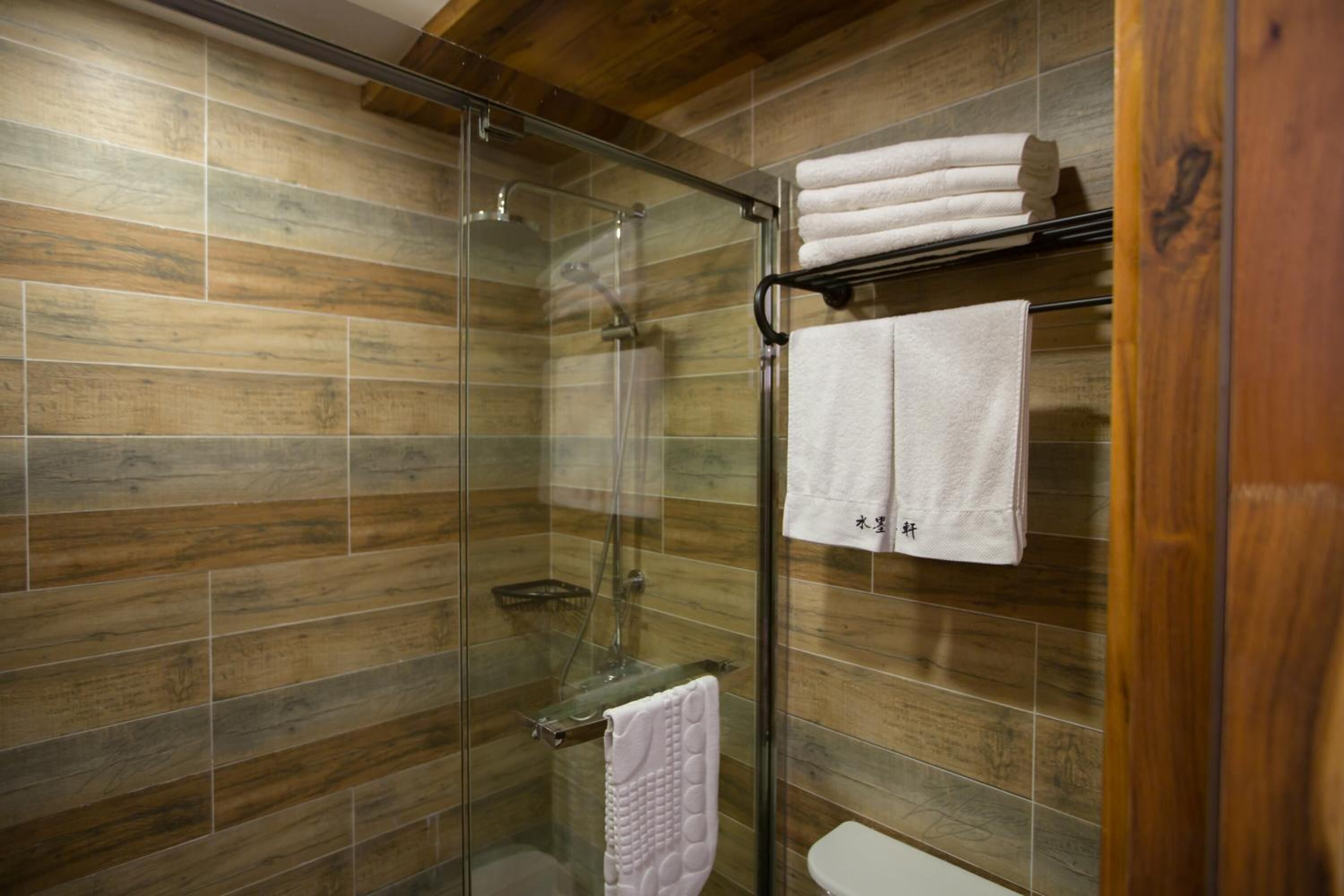 A modern bathroom with a glass shower enclosure, wooden wall tiles, and a toilet with a towel rack.