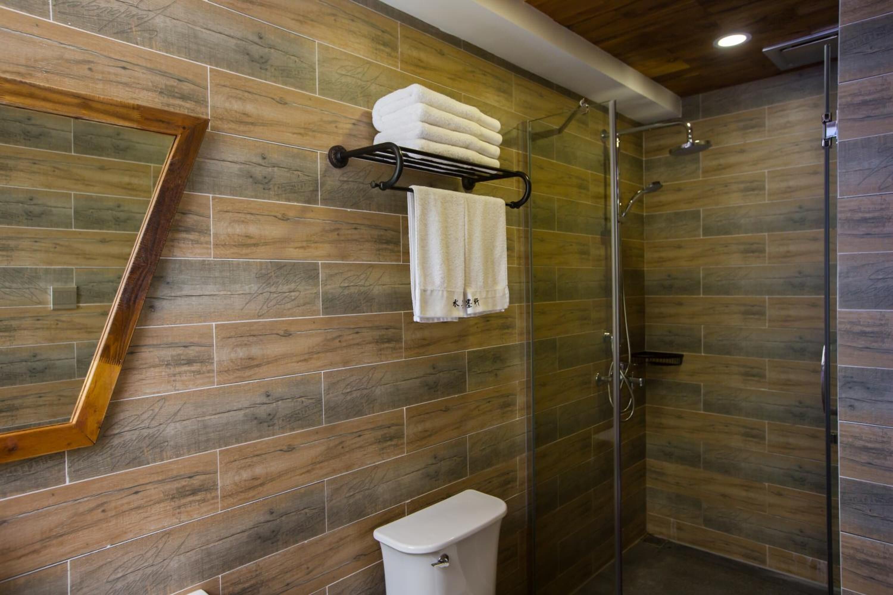 A bathroom with wooden wall tiles, a glass shower enclosure, and a toilet.