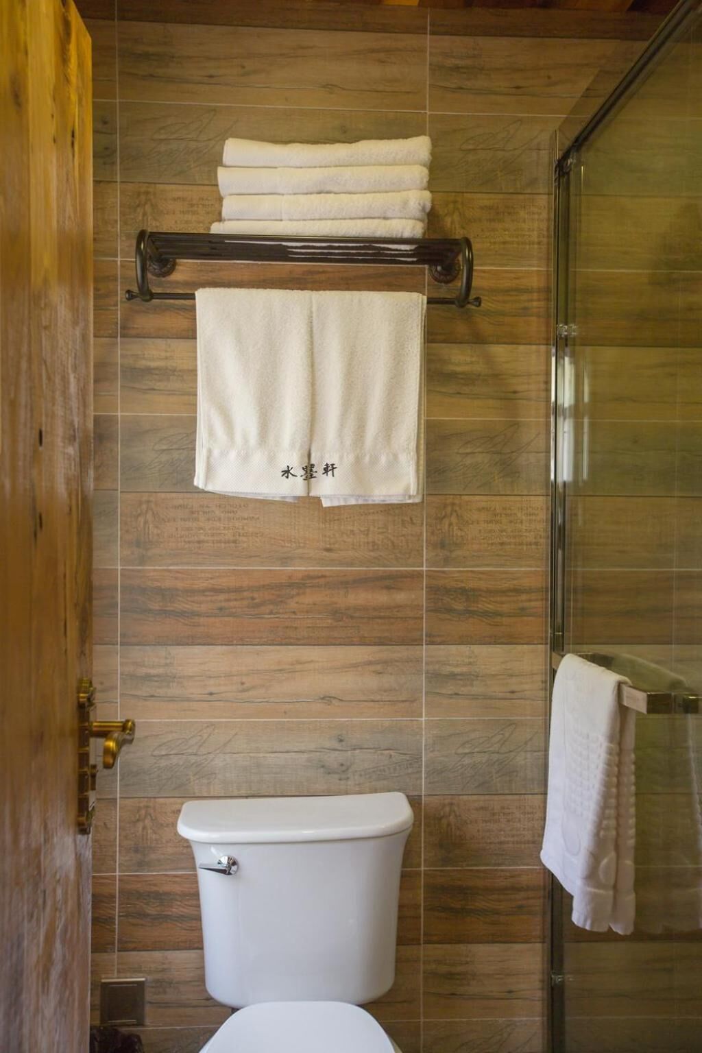 A bathroom with a wooden wall, a glass shower enclosure, and a white toilet.
