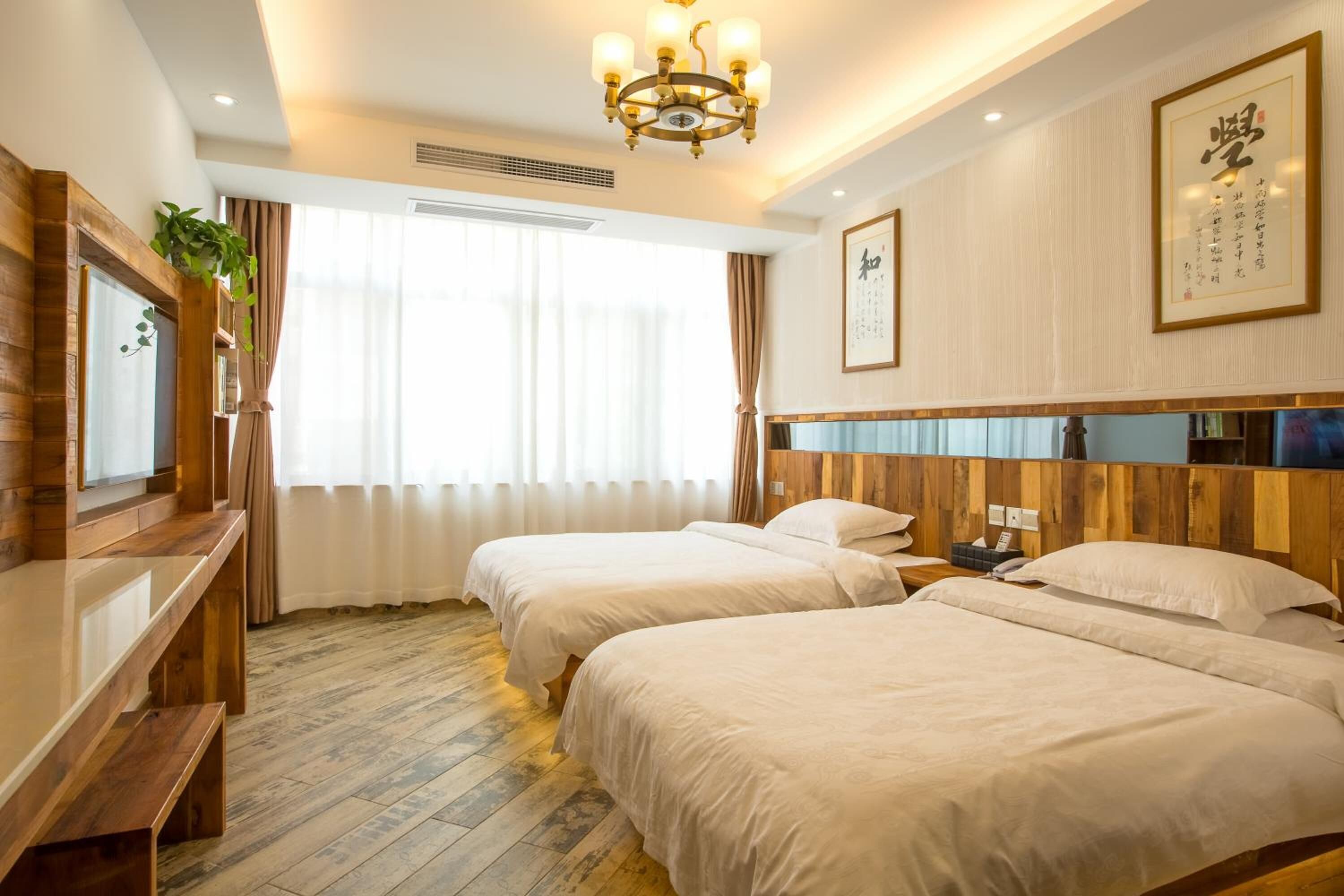 A hotel room with two beds, wooden headboard, a television, and a large window with curtains.