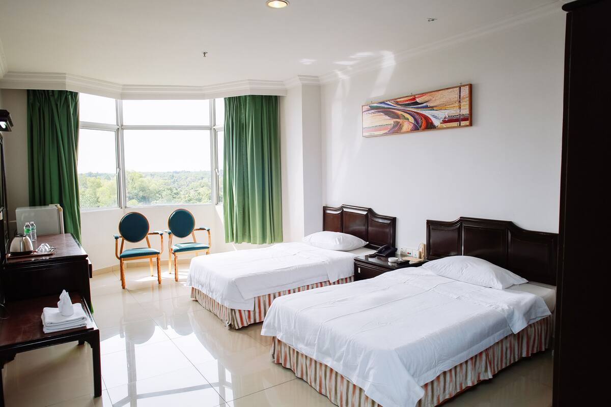 Une chambre d’hôtel avec deux lits, un bureau, des chaises, un tableau et une vue sur la verdure.