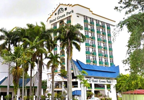 Un hotel de varios pisos llamado Hotel Green Park, con un letrero llamativo, rodeado de palmeras.