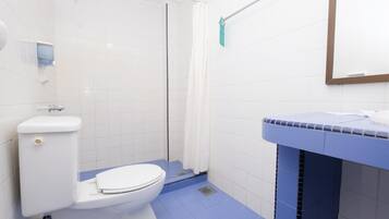 Un baño con inodoro blanco, ducha con cortina blanca y lavamanos con encimera azul.