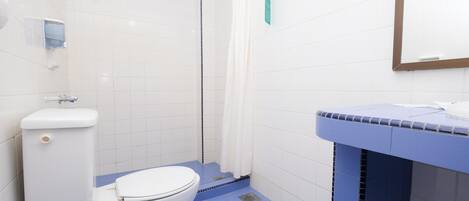 Ein Badezimmer mit Toilette, Dusche mit weißem Vorhang und Waschbecken mit blauer Ablagefläche.