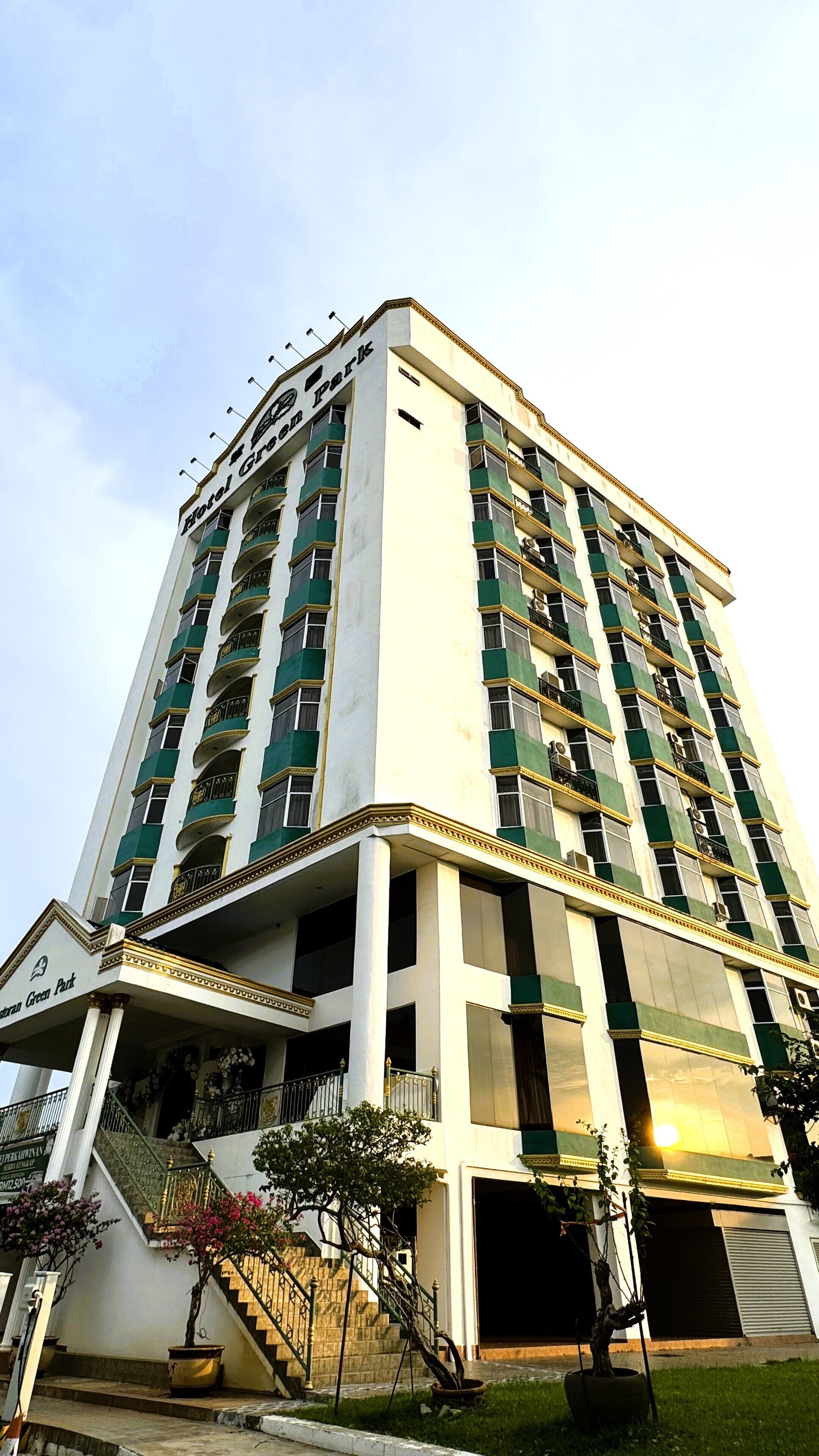 Un hotel alto con varios balcones, una escalera central y un letrero que dice "Hotel Green Park".
