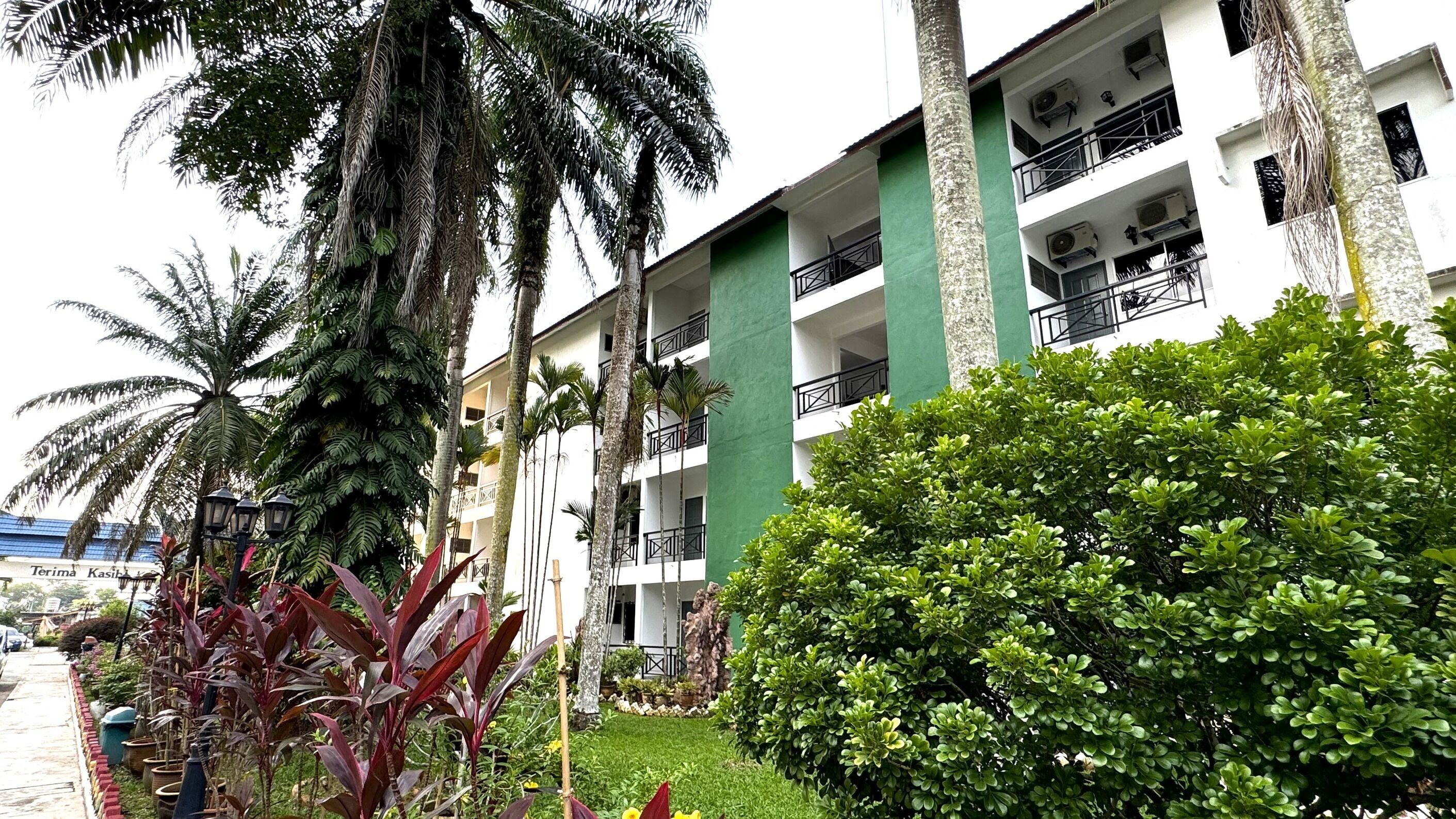 A multi-story hotel with balconies, surrounded by lush greenery and palm trees.