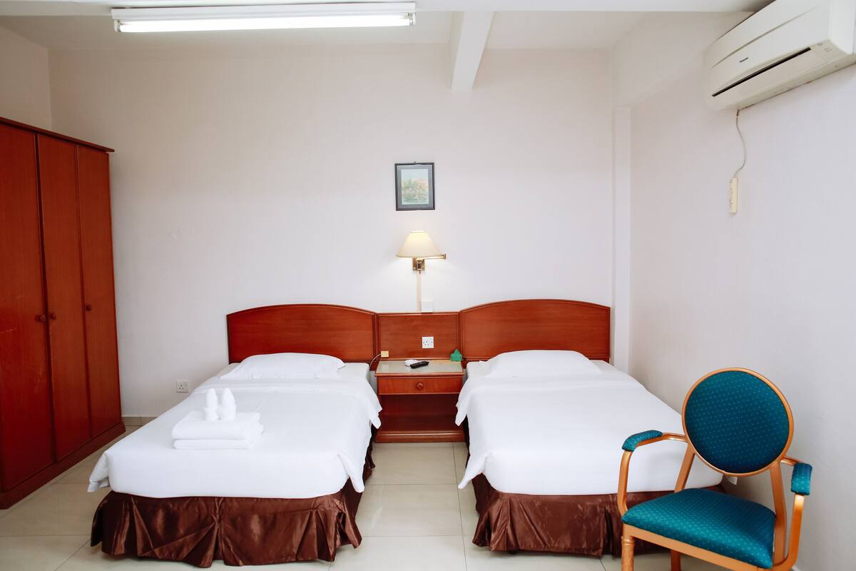 Une chambre d’hôtel avec deux lits, une armoire en bois, une table de chevet, une lampe et un appareil de climatisation.