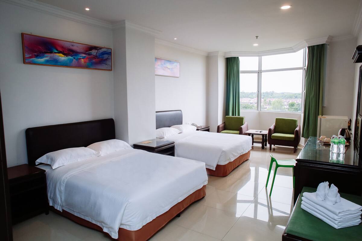 Une chambre d’hôtel avec deux lits, un bureau, une chaise, une table de chevet et une fenêtre avec des rideaux.