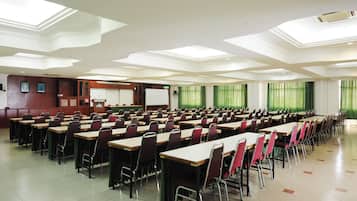 A large conference room with rows of tables and chairs, a whiteboard, and a projector screen.