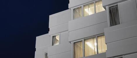 Un edificio de varios pisos con un estilo arquitectónico moderno, que presenta una serie de ventanas con cortinas.