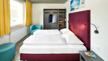 A modern hotel room with a large bed, a wardrobe, a seating area, and a view of the outdoors.