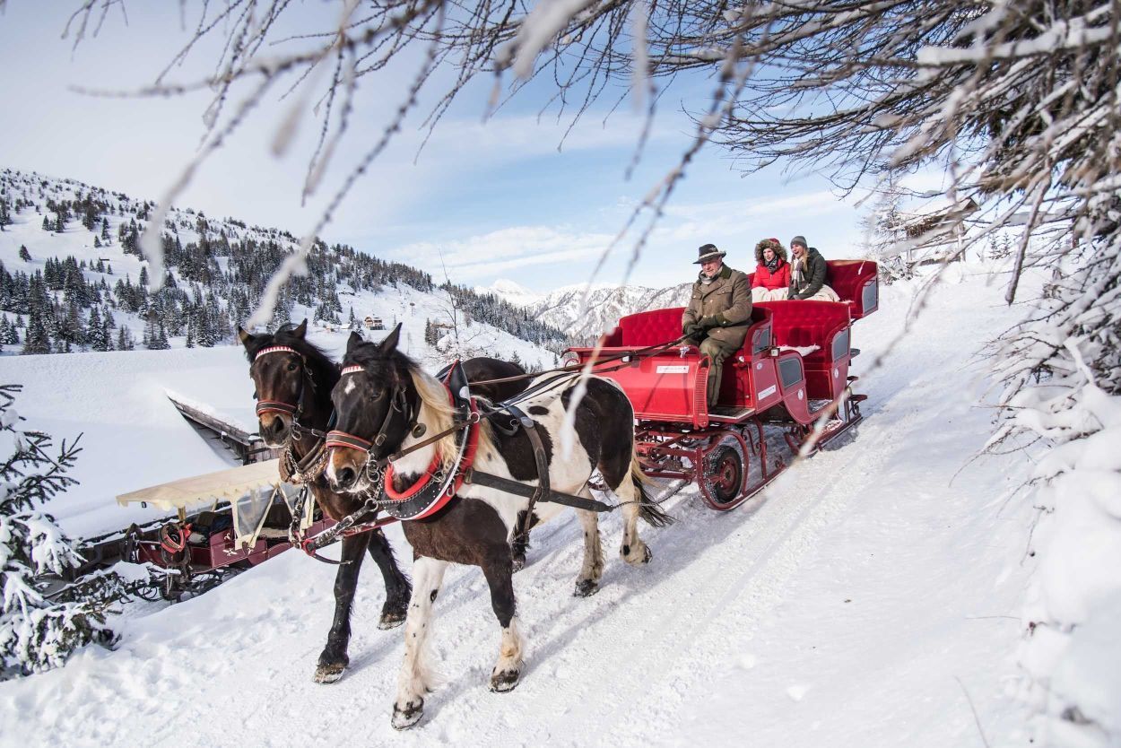 Uma charrete puxada por cavalos em um caminho coberto de neve, com passageiros.
