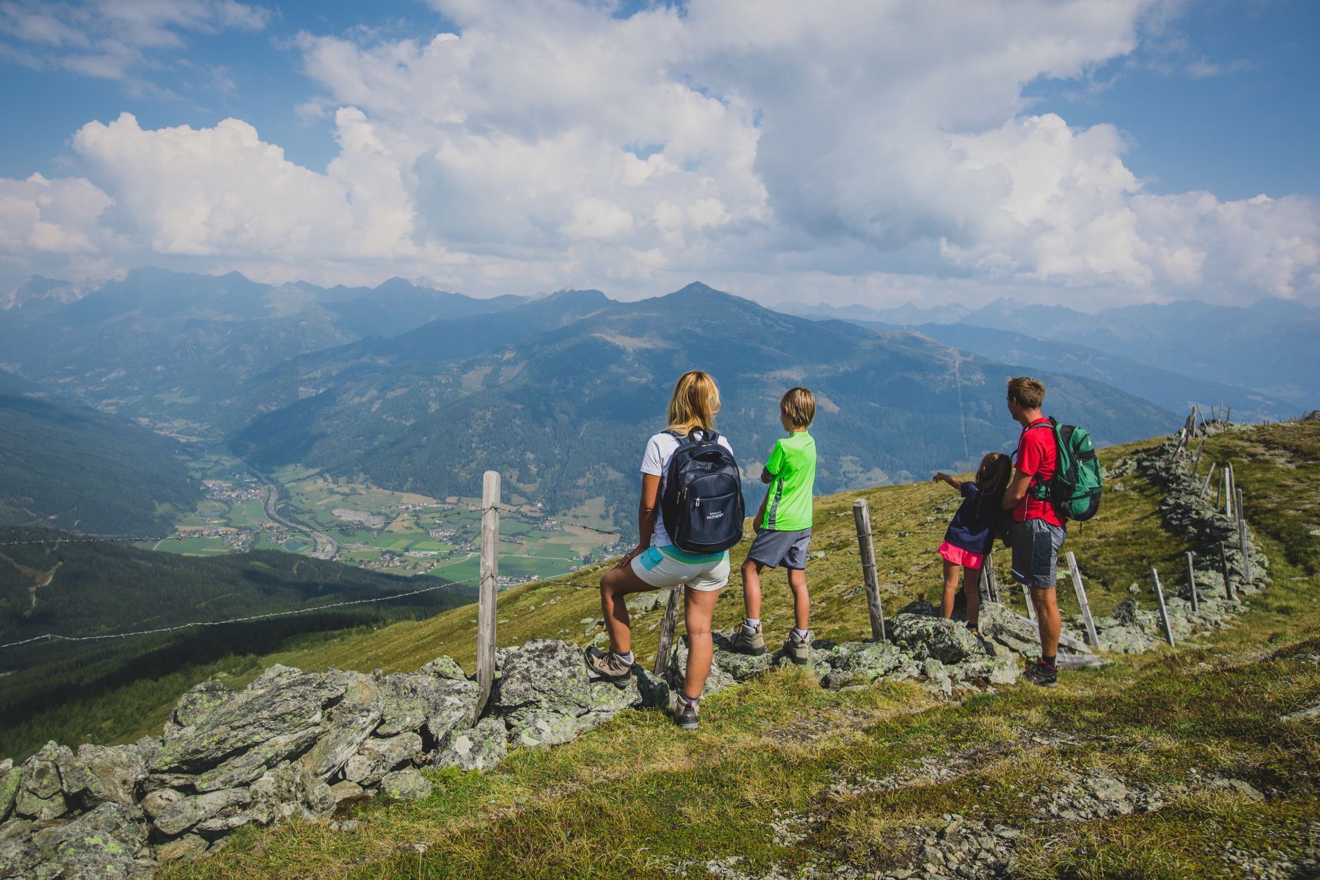 Un grupo de excursionistas en un sendero de montaña con vistas a un valle y montañas al fondo.