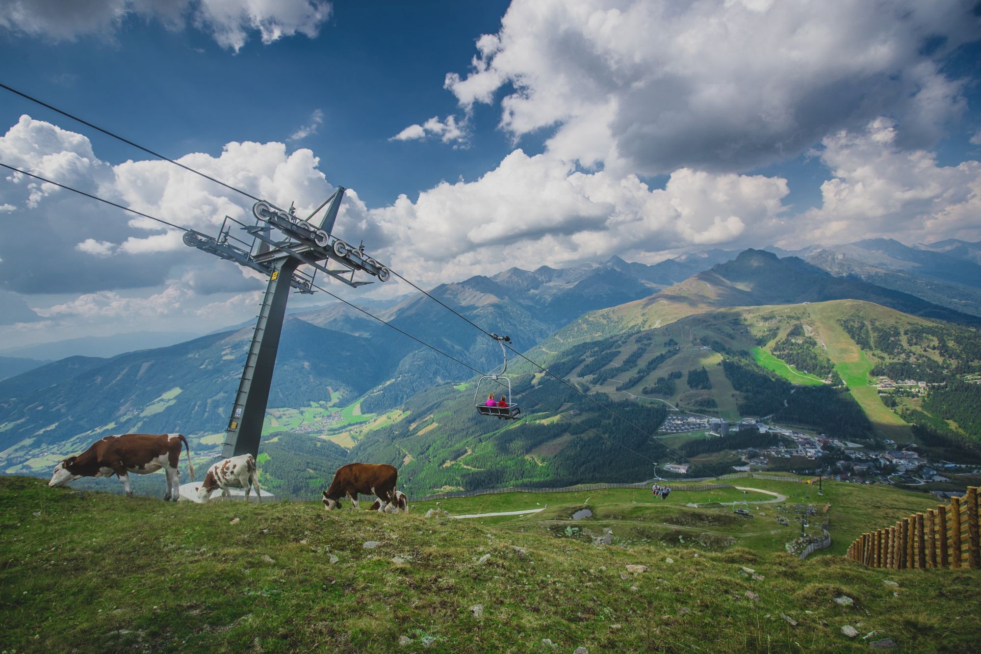 A mountain landscape with a cable car, cows grazing, and a village in the valley.