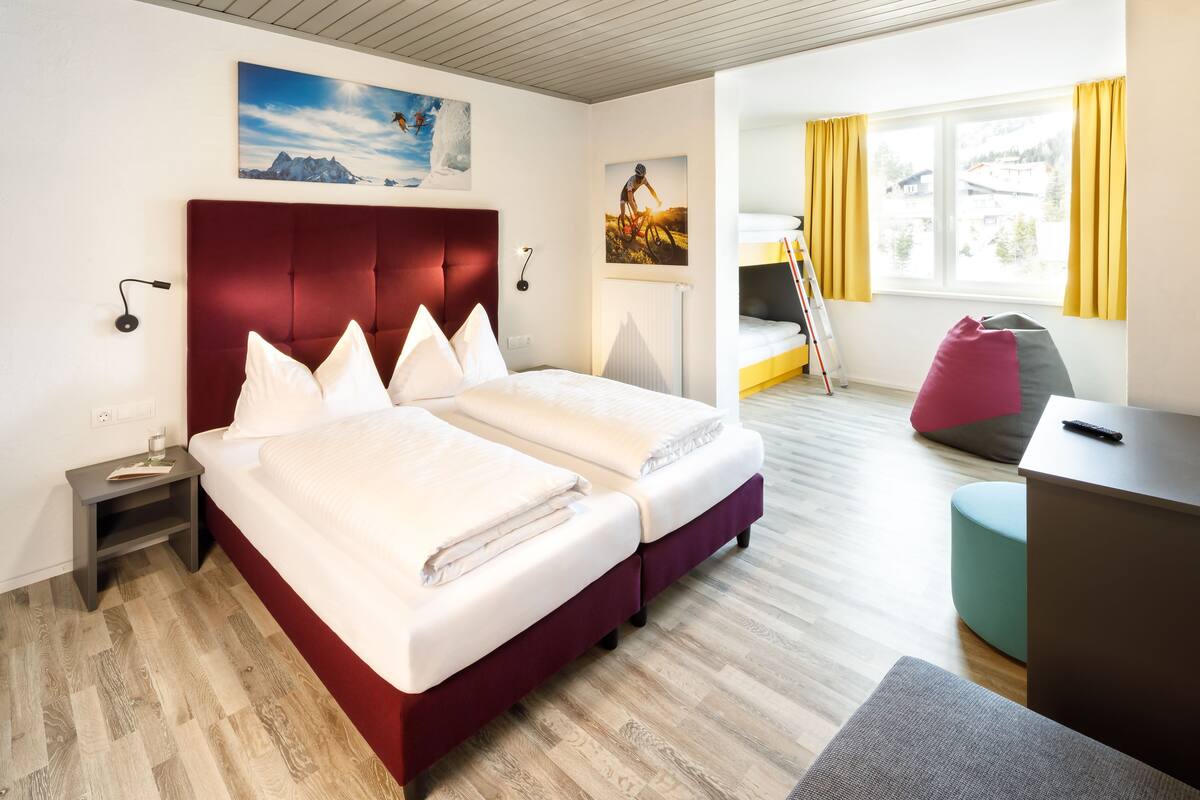 Ein Hotelzimmer mit einem großen Bett, einem Schreibtisch, einem Sessel und einem Fenster mit Vorhängen.
