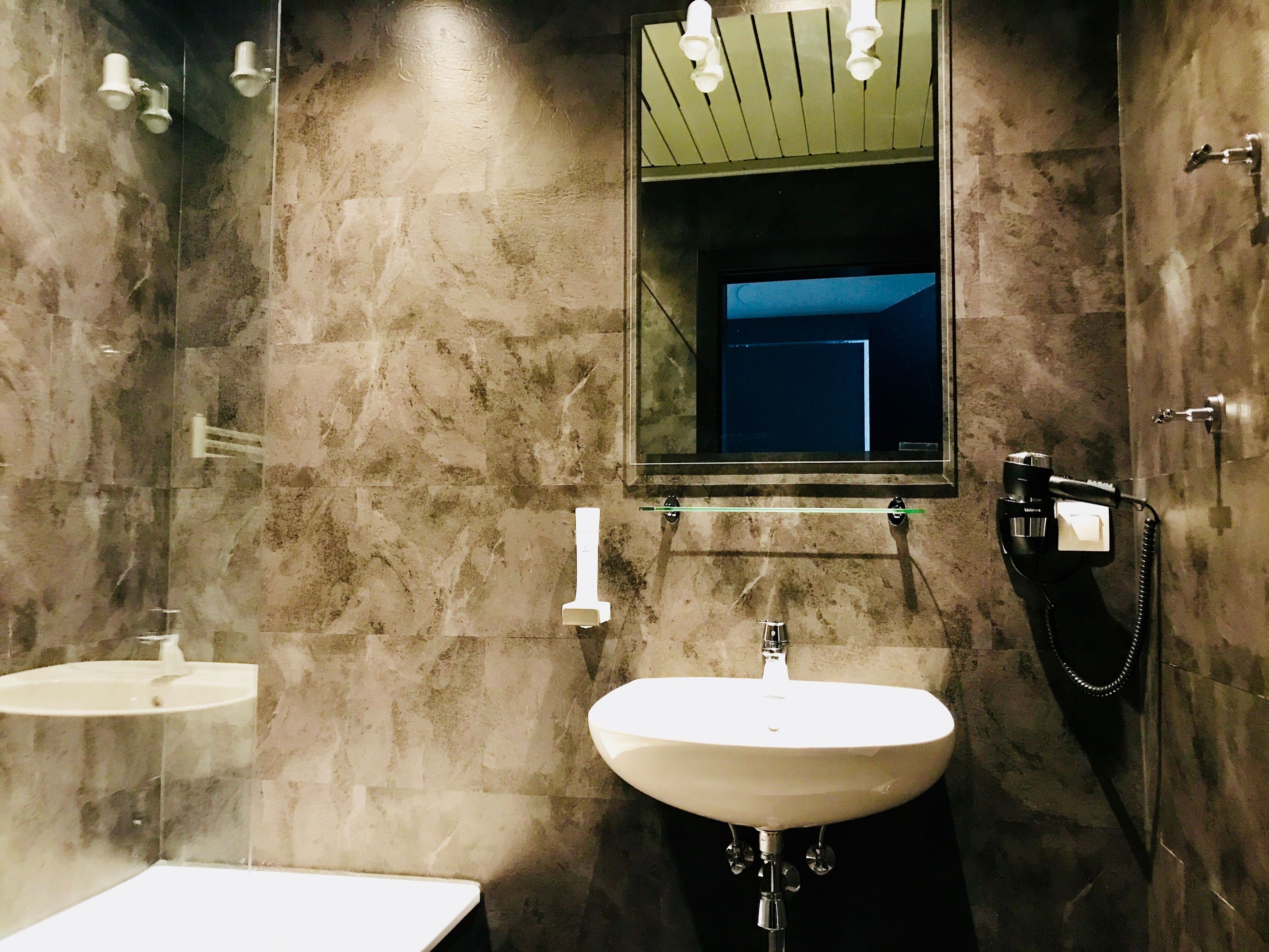 Un baño con pared de mármol, lavabo, espejo y secador de pelo.