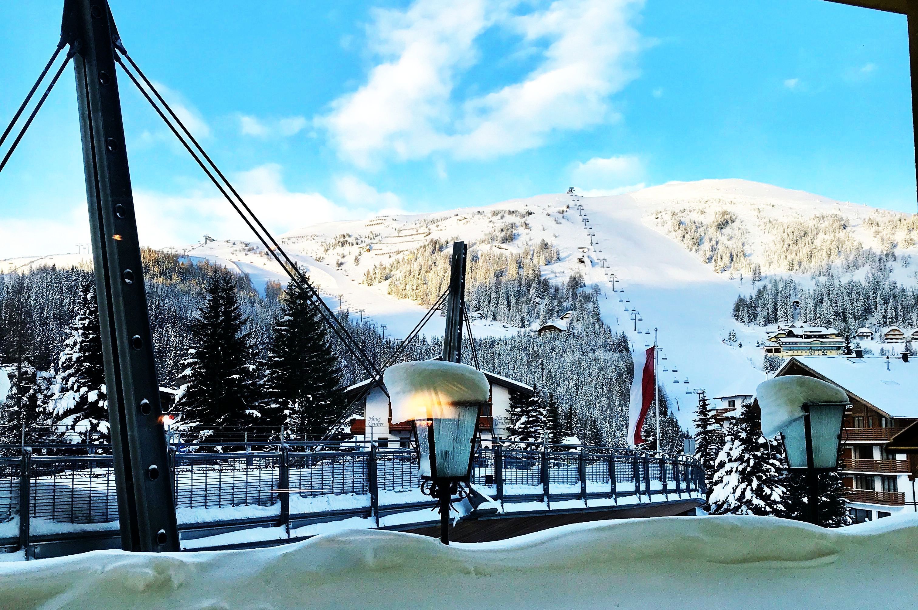 A snow-covered mountain with a ski lift and buildings in the background.