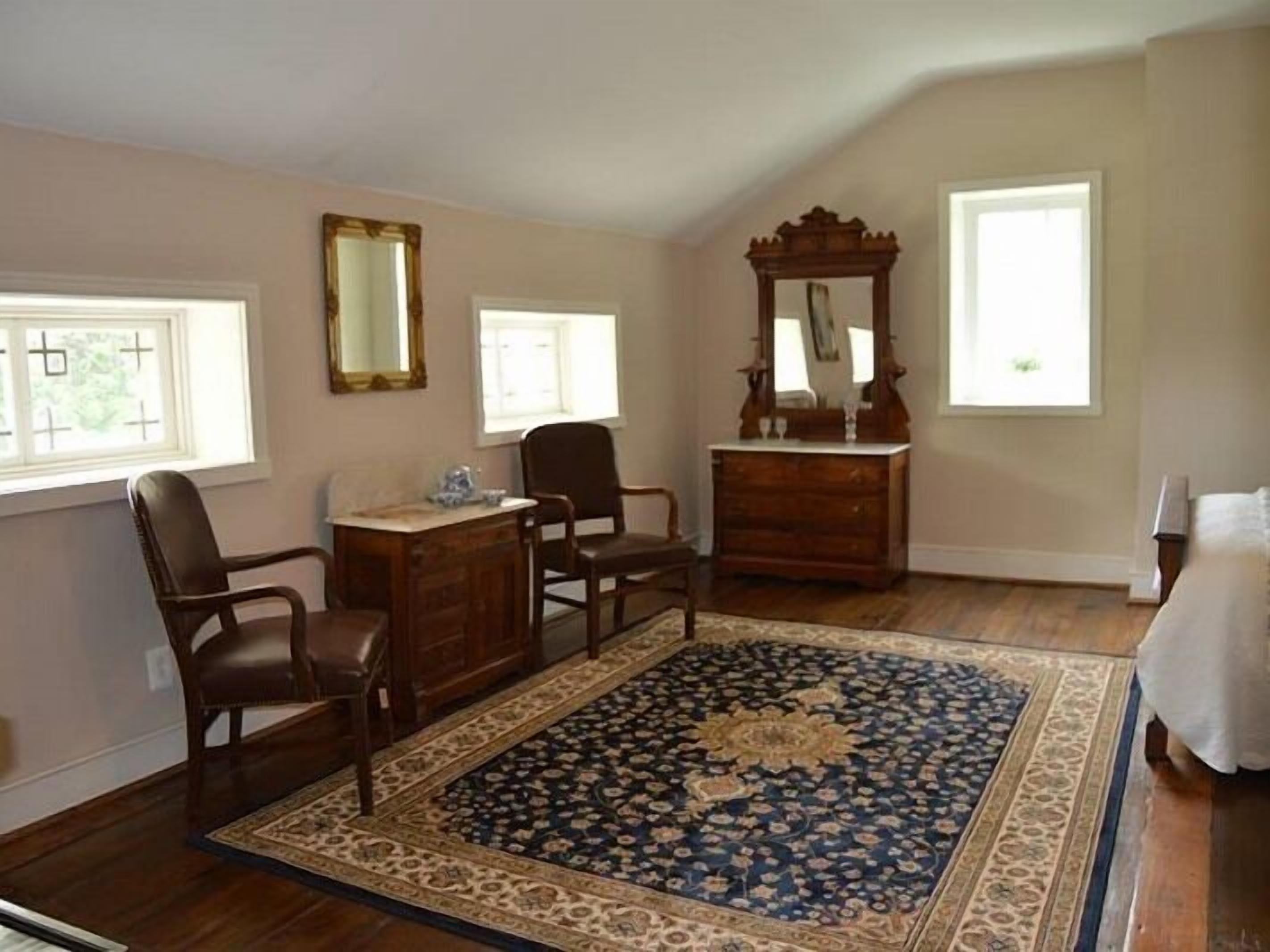 A bedroom with a bed, a dresser, a desk, two chairs, a large mirror, and a patterned rug.