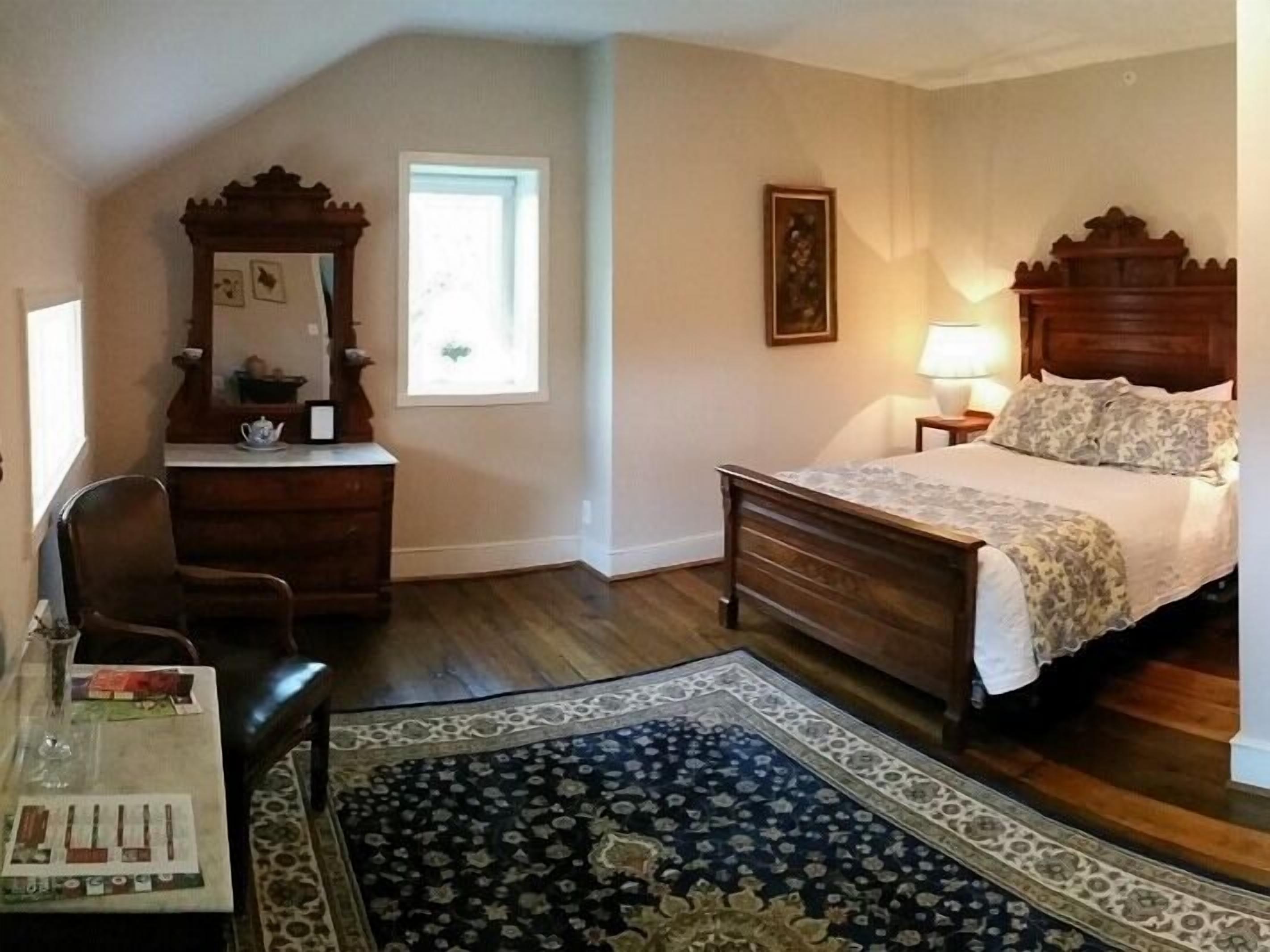 Une chambre à coucher avec un lit en bois, une table de chevet, une commode, un miroir et une fenêtre.