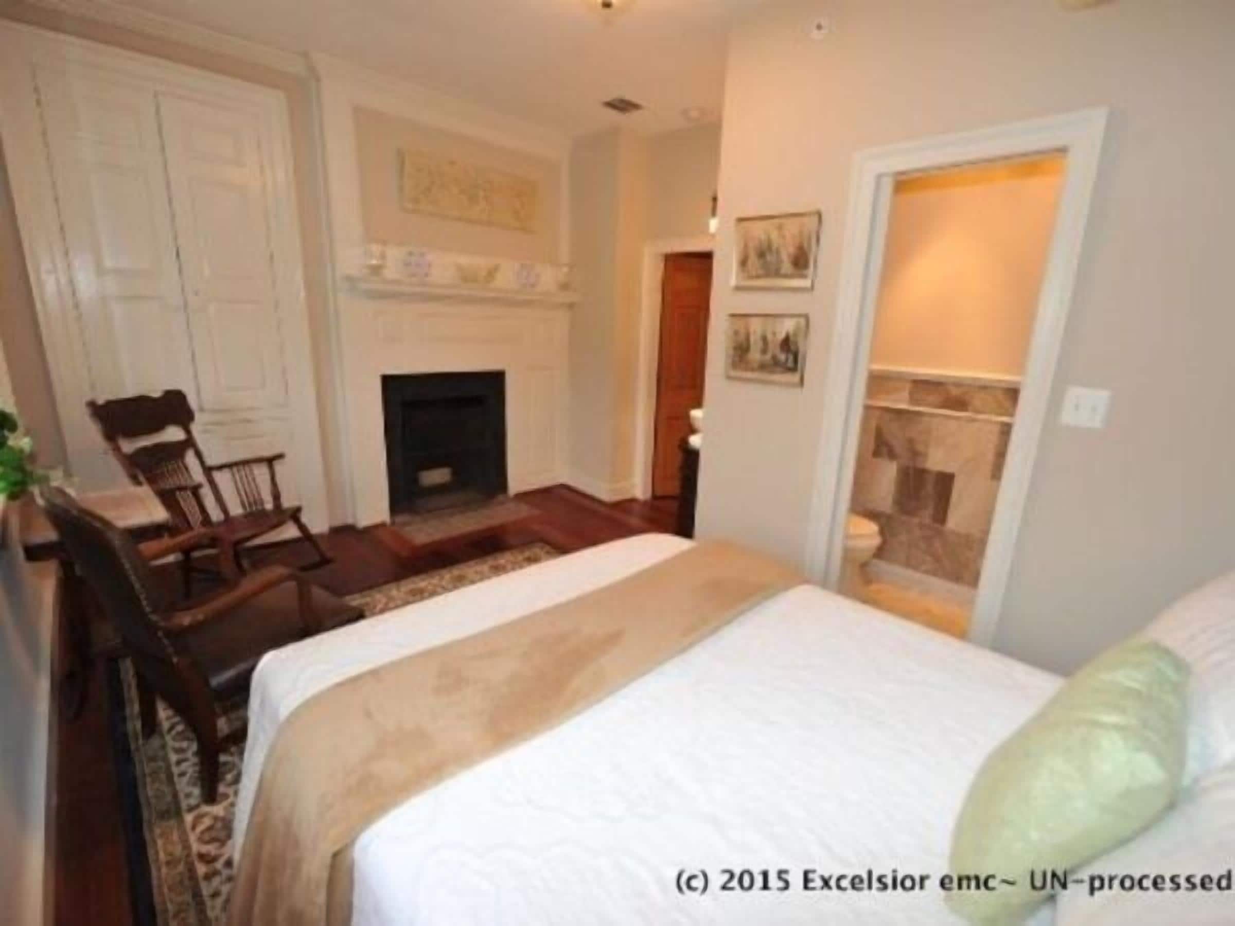 A bedroom with a bed, a chair, a fireplace, and a door leading to another room.