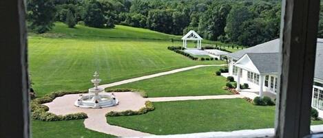 A view of a well-maintained lawn with a gazebo and a fountain, surrounded by a white building with large windows.