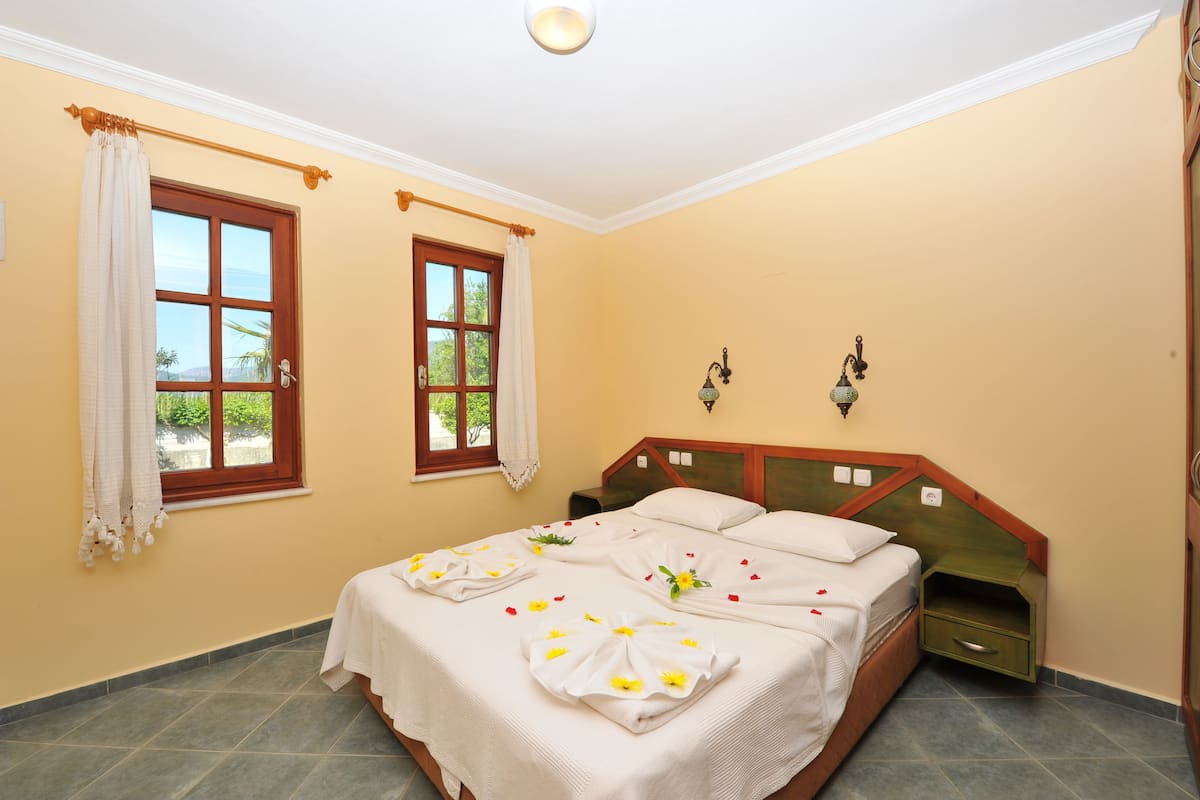 A bedroom with a bed, two windows, a nightstand, and a headboard.